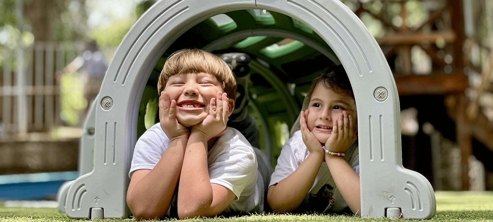 preschoolers smile underneath playground turtle structure